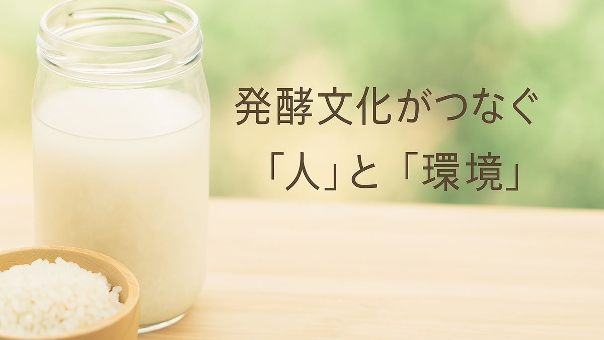 発酵中のどぶろくが入ったガラス瓶と米の入った木の器が木のテーブルに置かれ、背景には緑のぼかし。右寄に「発酵文化がつなぐ『人』と『環境』」の日本語テキストがある、優しい雰囲気の画像。